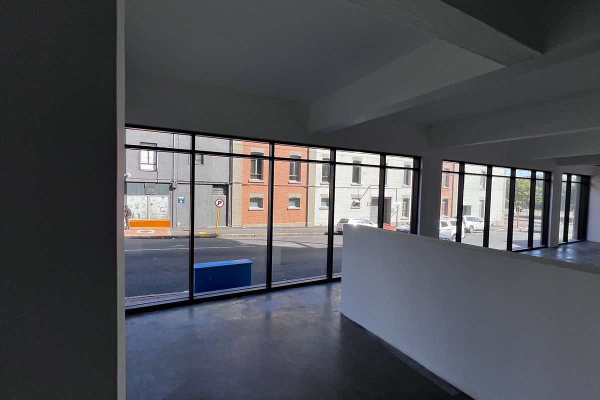 A bright, open-plan commercial office space featuring polished concrete floors, exposed structural beams, and expansive windows offering street-level views.