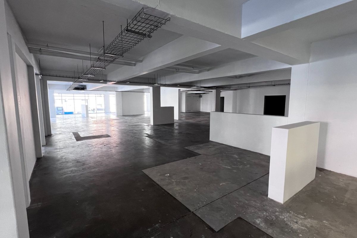 A spacious, open-plan commercial interior featuring exposed ceiling cable trays, structural columns, and raw concrete flooring, offering a versatile blank canvas for office fit-out.
