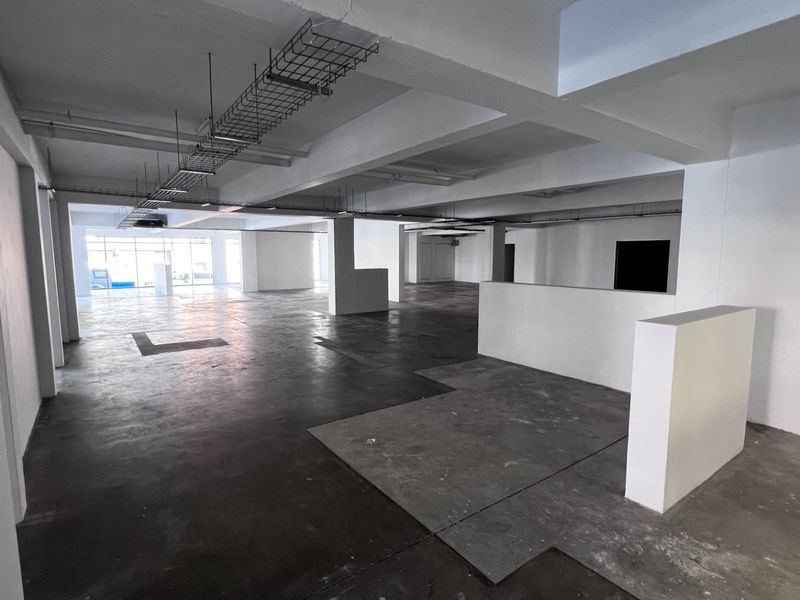 A spacious, open-plan commercial interior featuring exposed ceiling cable trays, structural columns, and raw concrete flooring, offering a versatile blank canvas for office fit-out.
