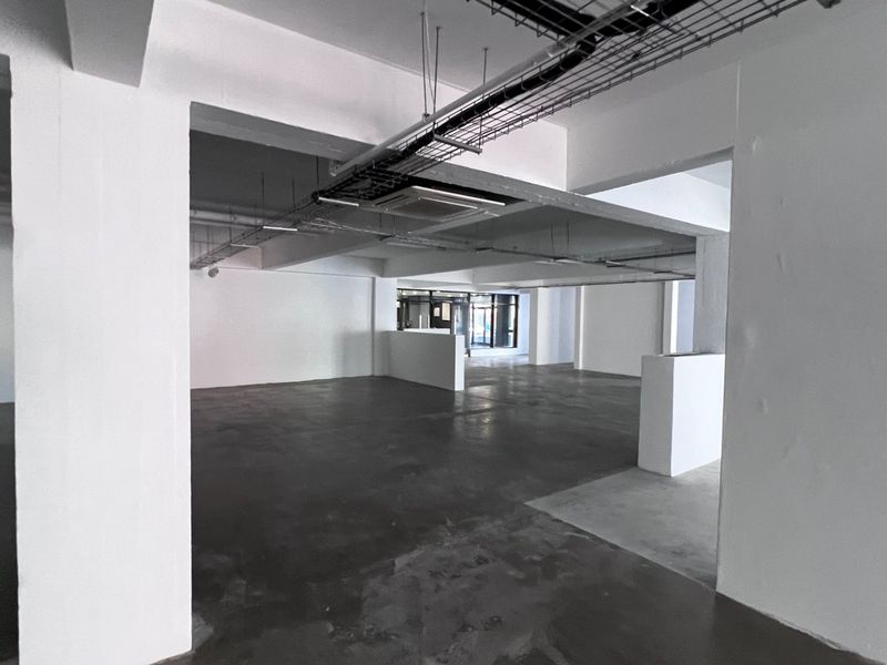 A spacious, open-plan commercial interior featuring exposed ceiling cable trays, concrete flooring, and structural columns, suitable for a versatile office or retail layout.