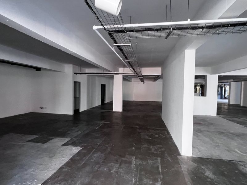 A large, open-plan commercial space featuring exposed ceiling services, structural columns, and unfinished concrete flooring, suitable for custom office or retail fit-out.