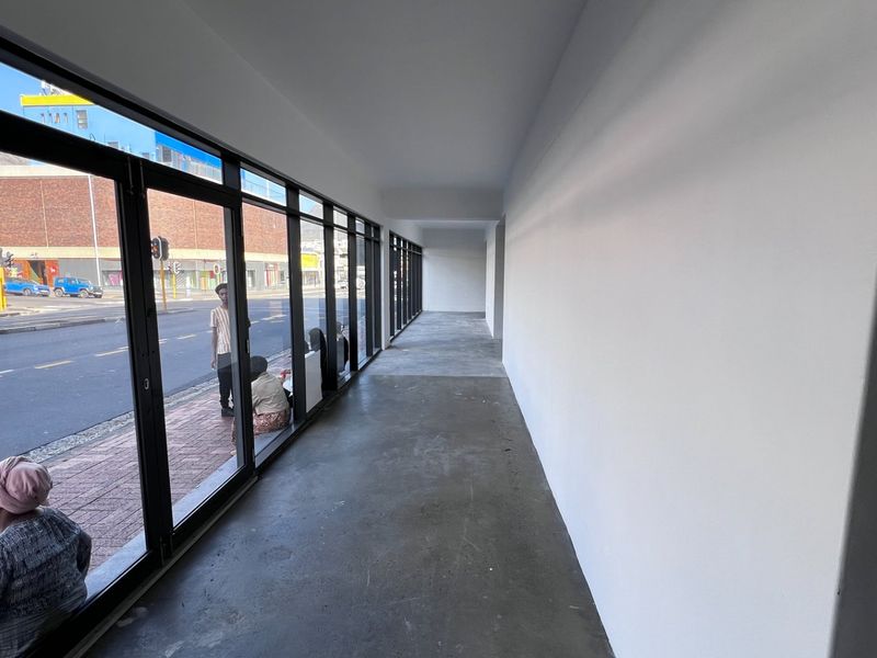 A bright, modern hallway featuring polished concrete floors and expansive floor-to-ceiling glass folding doors providing excellent natural light and street views.