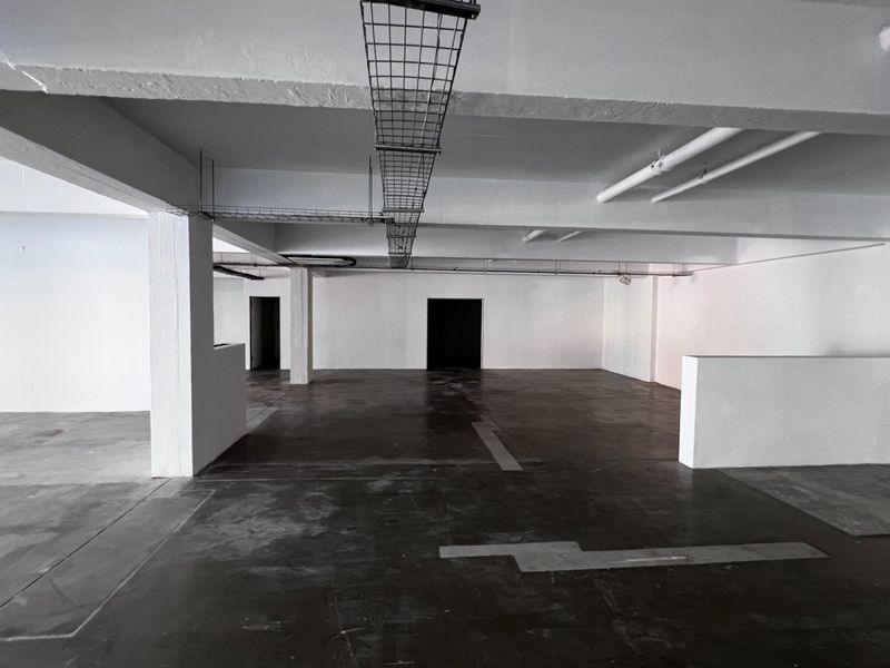 An expansive, open-plan commercial utility or storage space featuring exposed industrial ceiling infrastructure, concrete flooring, and structural columns.