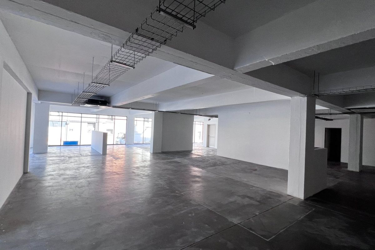 Spacious open-plan commercial area featuring exposed concrete ceilings, cable trays, polished concrete floors, and large windows providing ample natural light.