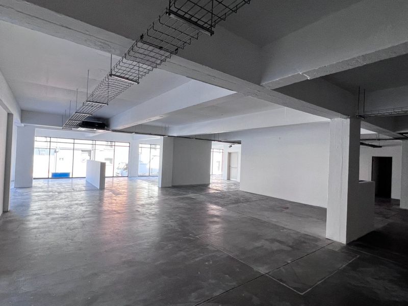Spacious open-plan commercial area featuring exposed concrete ceilings, cable trays, polished concrete floors, and large windows providing ample natural light.