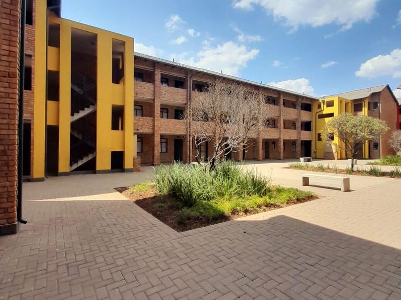 A view of the communal courtyard featuring brick-paved walkways, landscaped garden beds, and multi-story residential blocks with exposed brick and yellow accents.