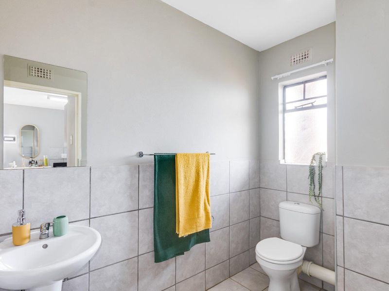 A functional bathroom featuring a pedestal basin, toilet, and neutral wall tiling with a window for natural light.