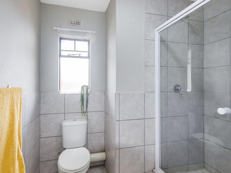 A clean, functional bathroom featuring a glass-enclosed shower, a standard toilet, and neutral grey wall and floor tiling.