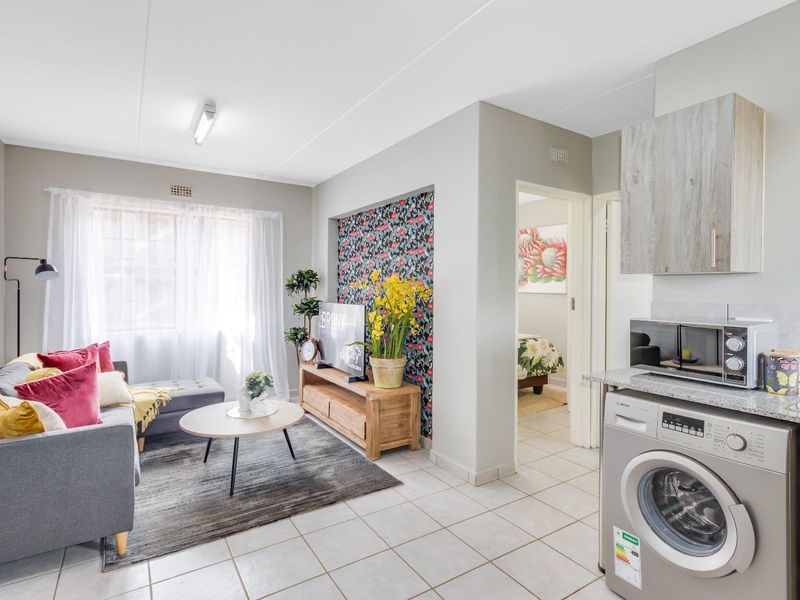 Open-plan living area featuring tiled flooring, a compact kitchen with built-in cabinetry, stone countertops, and integrated laundry appliances.