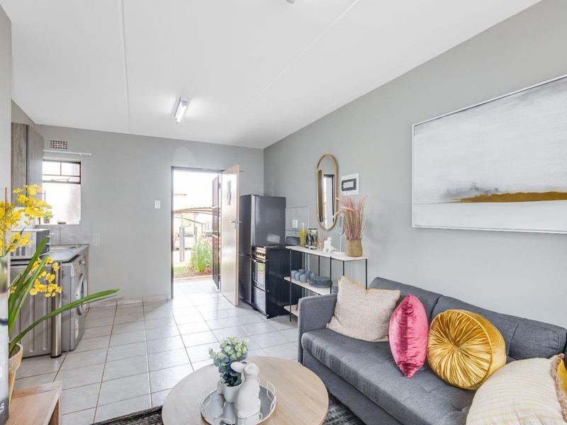 An open-plan living area featuring tiled flooring, a compact kitchen section with built-in cabinetry, and direct access to the exterior.