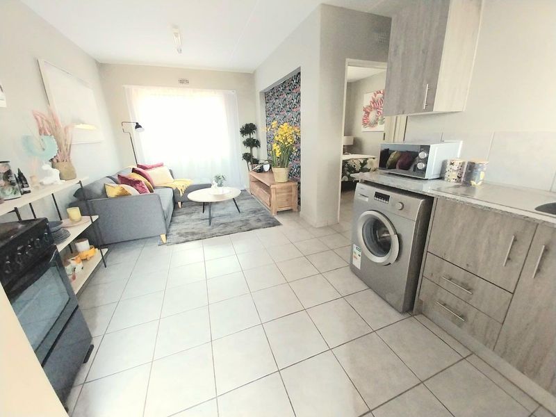 Open-plan living area featuring tiled flooring, integrated kitchen cabinetry with built-in oven, and laundry plumbing, creating a functional and connected living space.