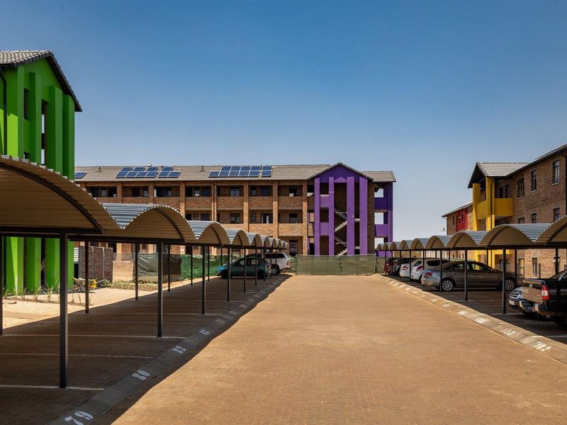 A well-maintained residential complex featuring paved parking areas with covered bays and solar panels installed on the building roofs.