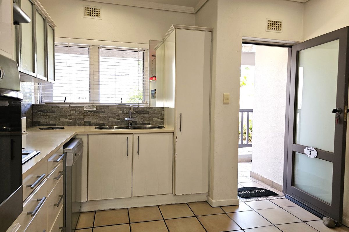 A functional kitchen featuring built-in cabinetry, a double sink, stone-look backsplash, and tiled flooring, with direct access to an outdoor area.