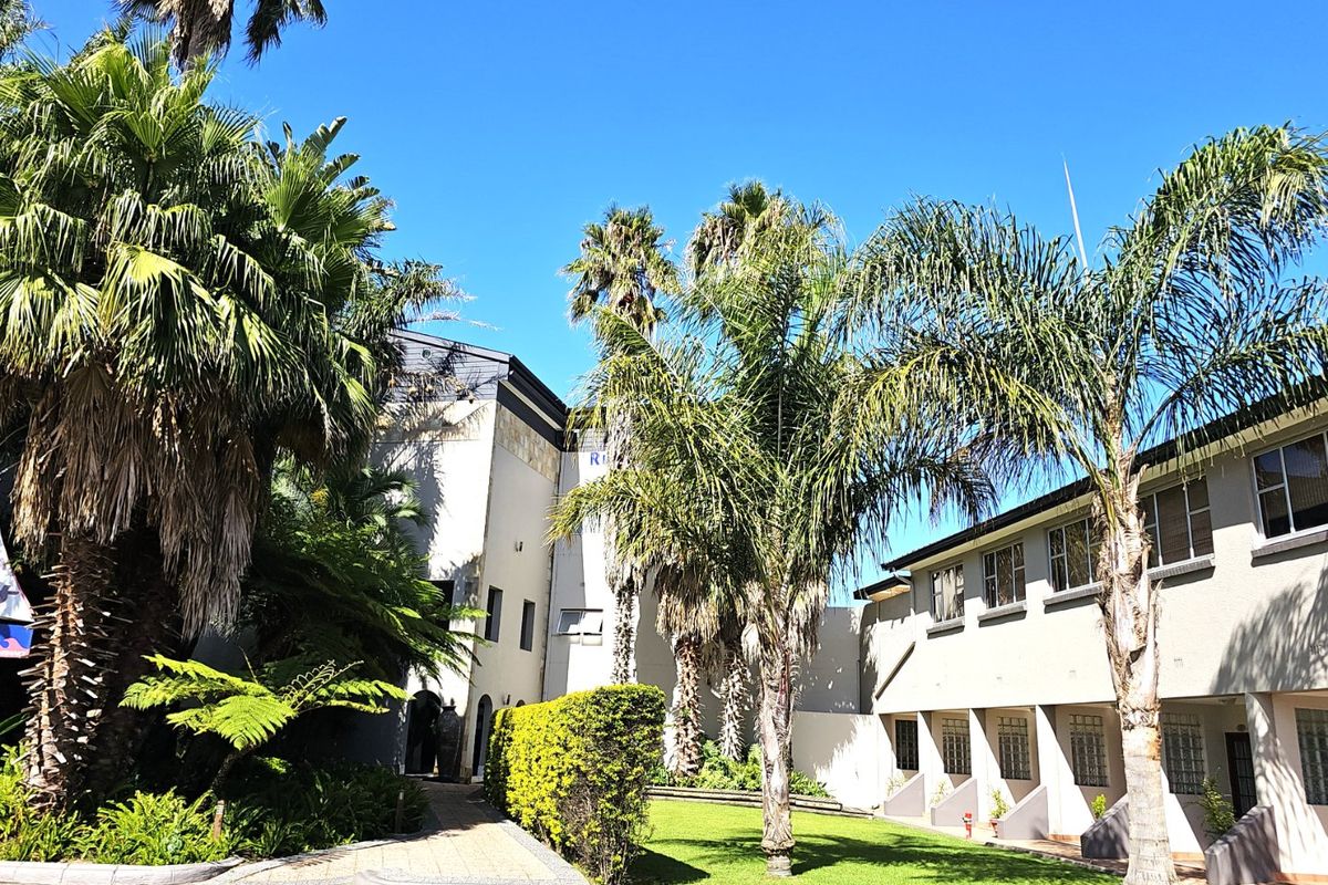 A well-maintained commercial property exterior featuring a landscaped garden, mature palm trees, and a paved walkway leading to the building entrance.