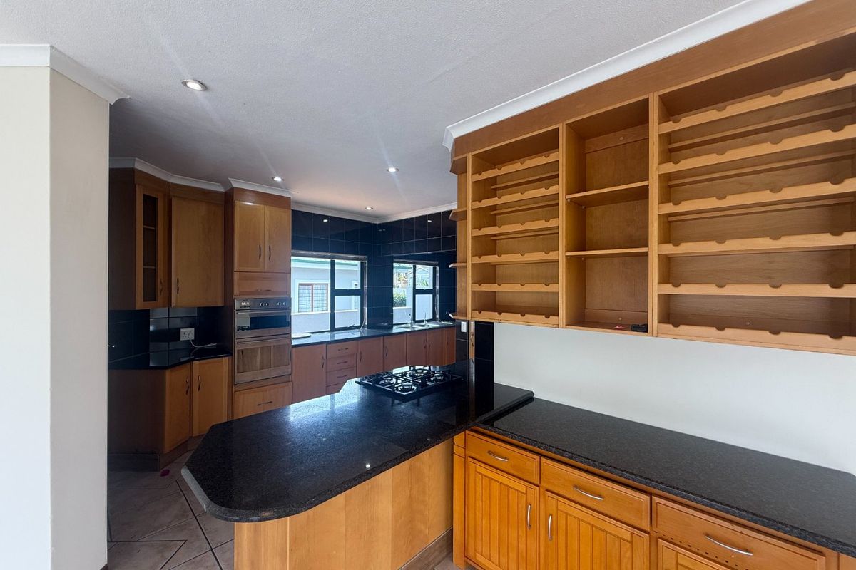 Spacious kitchen featuring extensive wooden cabinetry, granite countertops, built-in oven, gas hob, and dedicated wine storage shelving.