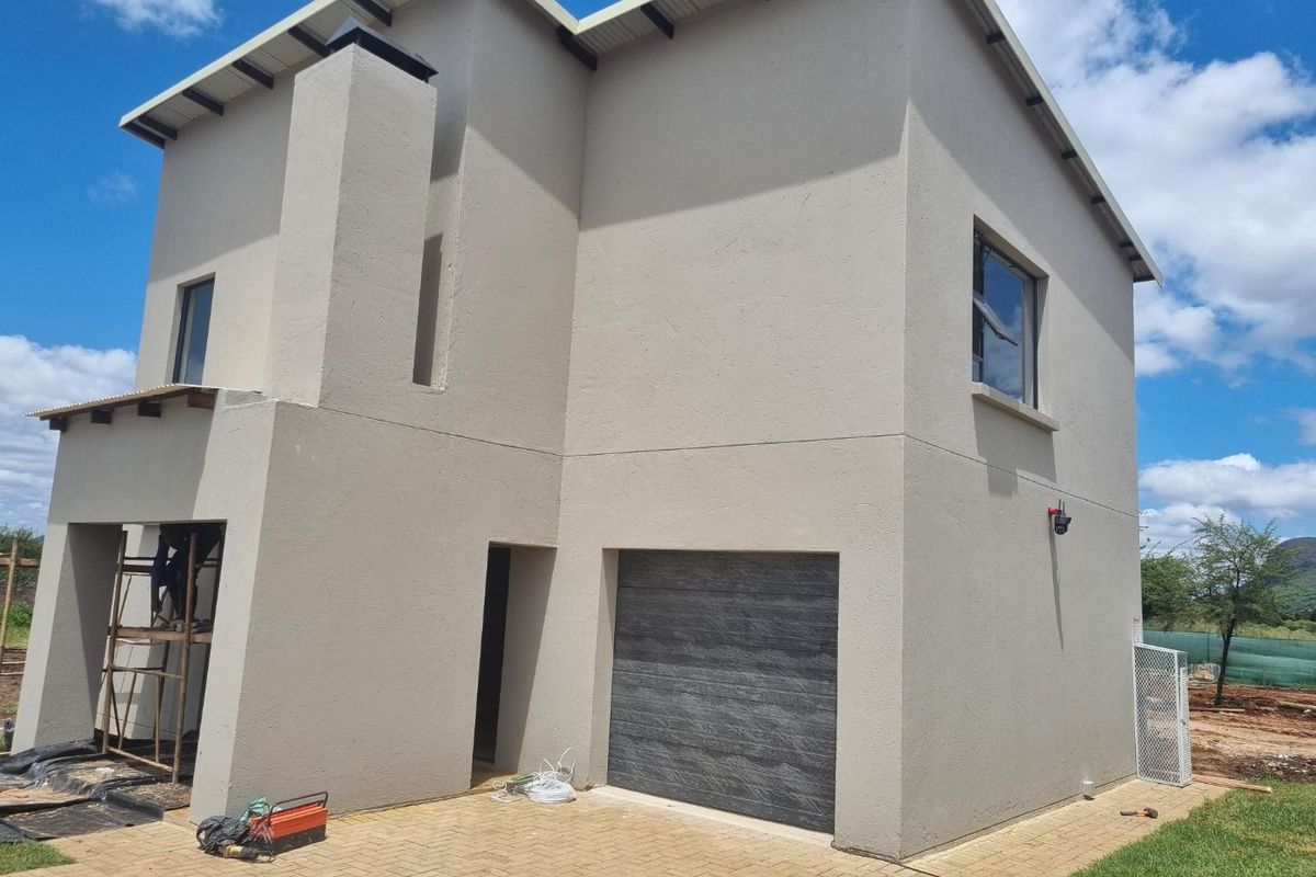 Exterior view of a modern townhouse featuring a textured garage door, smooth rendered facade, and paved driveway area under construction.