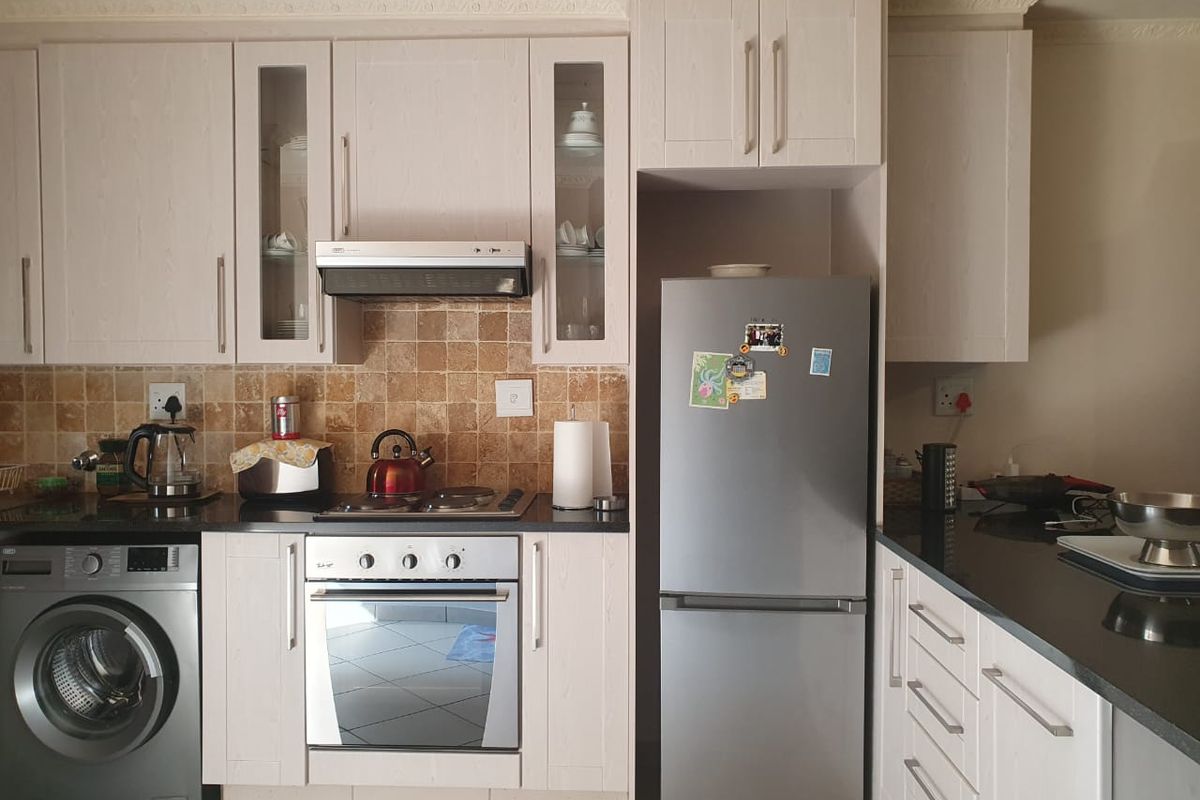 A functional kitchen featuring light-toned cabinetry, granite countertops, a tiled backsplash, and integrated appliances including an oven and extractor fan.