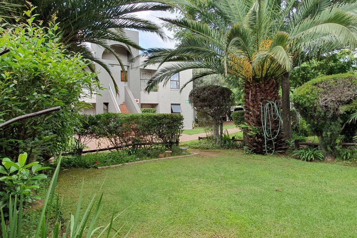 A well-maintained communal garden area featuring a lush lawn, mature palm trees, and established hedging, providing a pleasant outdoor space for residents.