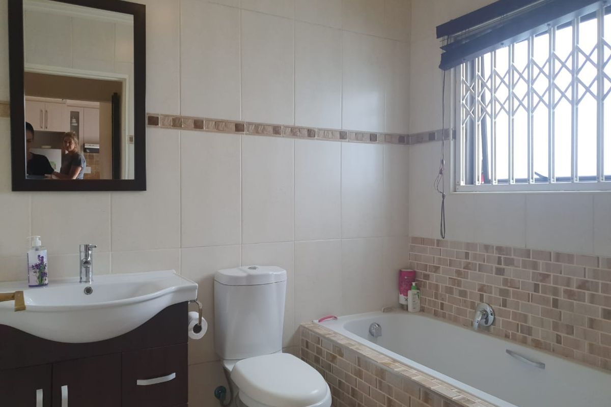A functional bathroom featuring a vanity cabinet with basin, a built-in bathtub with tiled surround, and a window with security gate.