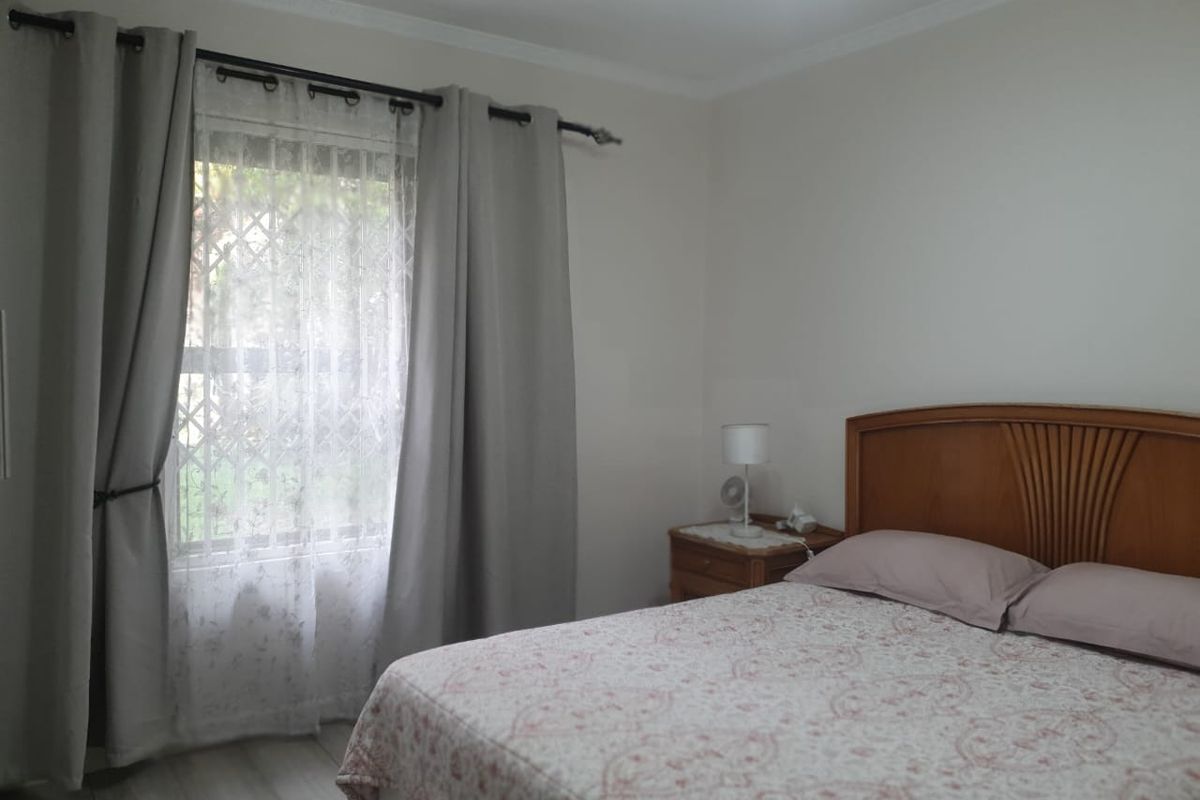 A well-lit bedroom featuring laminate flooring, decorative ceiling cornicing, and a window fitted with a security gate.