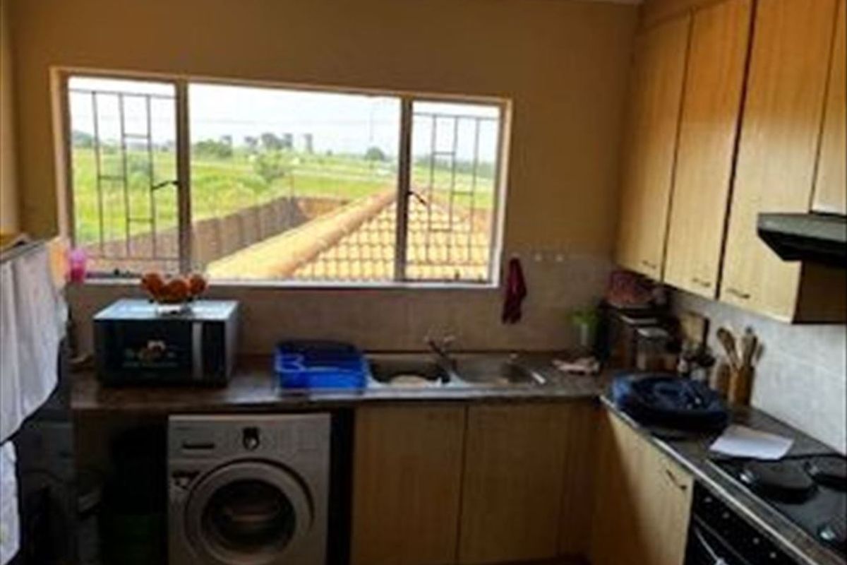 A functional kitchen featuring laminate cabinetry, built-in oven with hob, extractor fan, and a window with security bars overlooking the exterior.