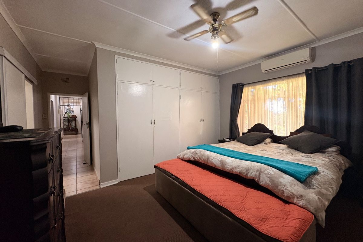 A spacious bedroom featuring built-in cupboards, a ceiling fan, and a wall-mounted air conditioning unit, with direct access to an adjacent hallway.