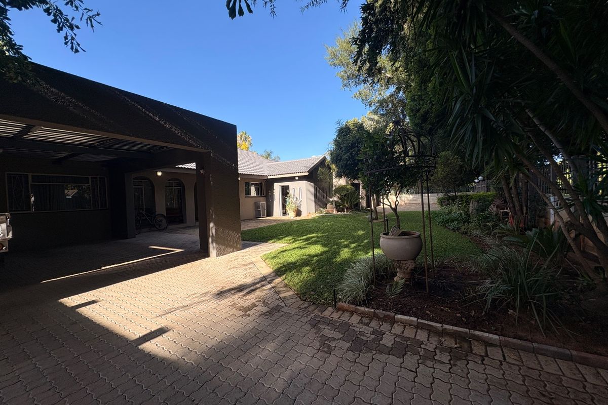 A well-maintained rear exterior view featuring a paved driveway, covered carport, and a lush green garden area.