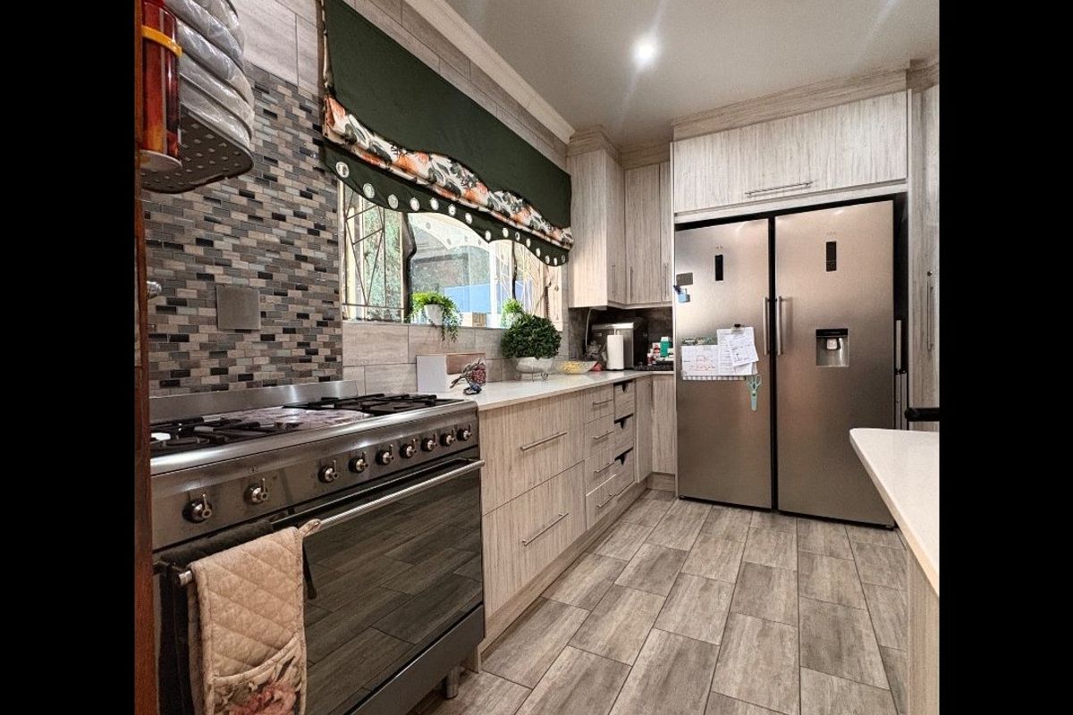 Modern kitchen featuring wood-look cabinetry, stone countertops, a mosaic tile backsplash, and a stainless steel gas stove with oven.