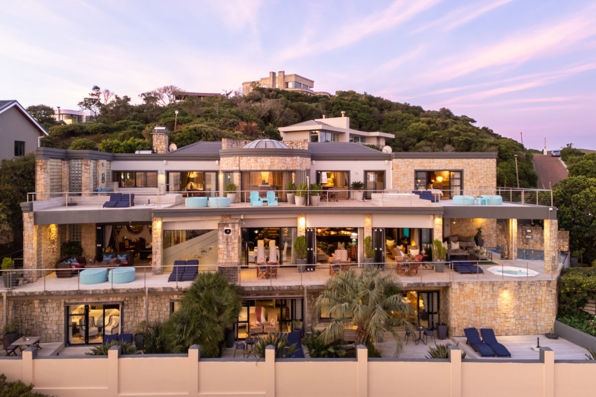 Expansive multi-level rear facade featuring stone cladding, extensive glass sliding doors, multiple balconies, and a built-in spa overlooking the landscaped grounds.