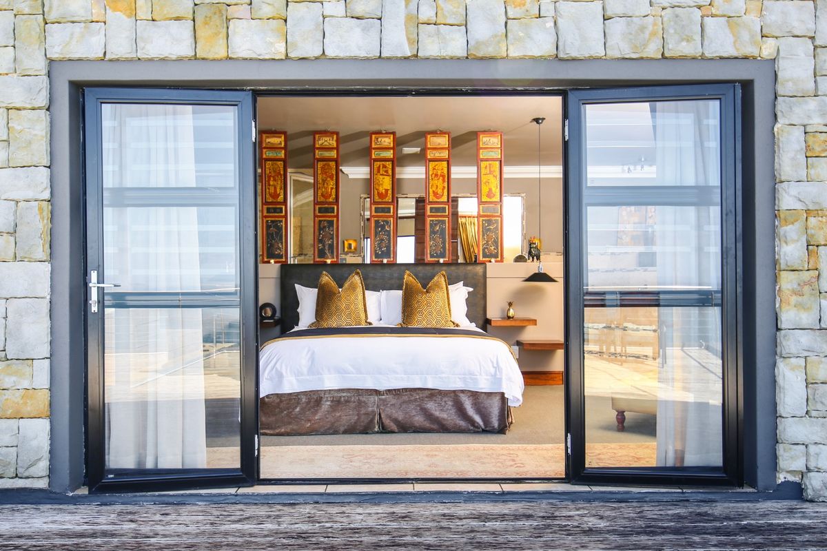 A view into a well-appointed bedroom featuring stone exterior cladding, modern aluminium glass doors, and direct access to a timber deck.