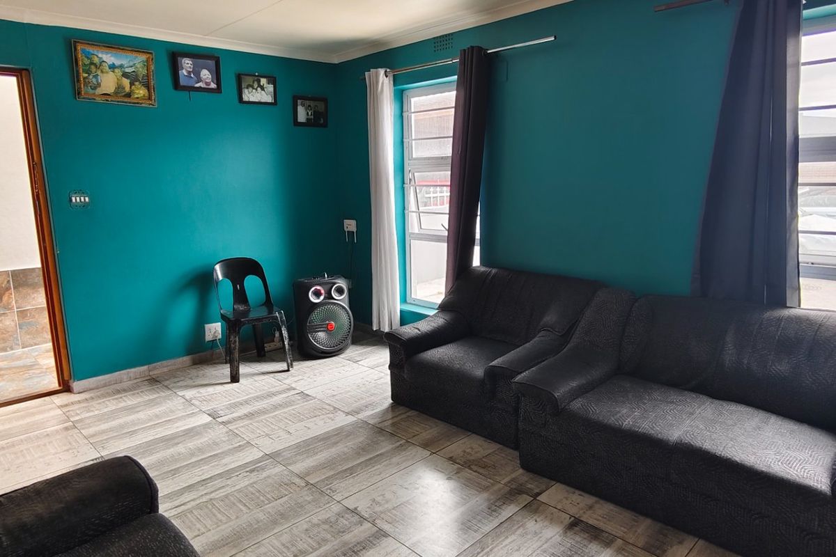 A living room featuring tiled flooring and aluminium window frames, providing a functional space with direct access to an adjacent tiled area.