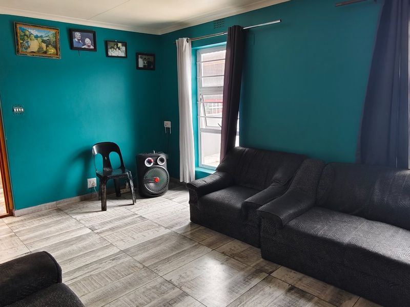 A living room featuring tiled flooring and aluminium window frames, providing a functional space with direct access to an adjacent tiled area.