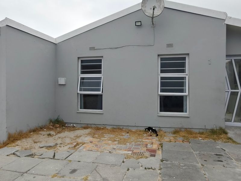 Front elevation of a single-story house featuring a roller garage door, aluminium windows with security bars, and a paved driveway area requiring maintenance.