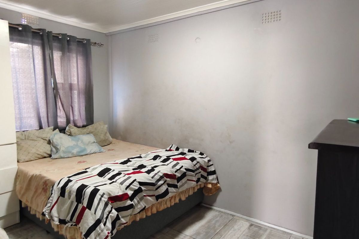 A bedroom featuring laminate flooring, a built-in wardrobe, and cornicing. The walls show visible signs of staining and surface wear.