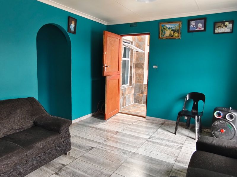 A living room featuring tiled flooring, an arched doorway, and direct access to an exterior area through a wooden door.