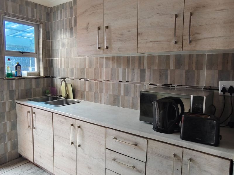 A functional kitchen featuring light wood-grain cabinetry, laminate countertops, a stainless steel double sink, and modern tiled wall finishes.