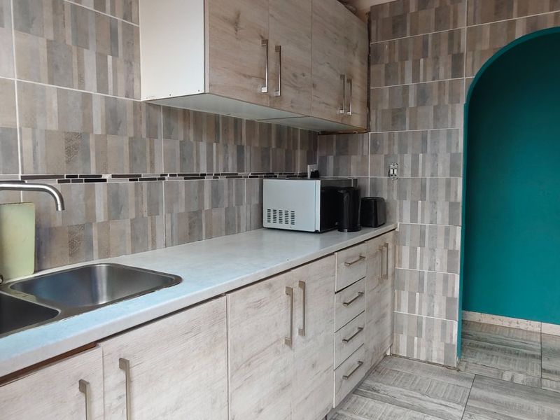 A functional kitchen featuring wood-look cabinetry, laminate countertops, a stainless steel double sink, and tiled finishes with a distinctive arched entryway.