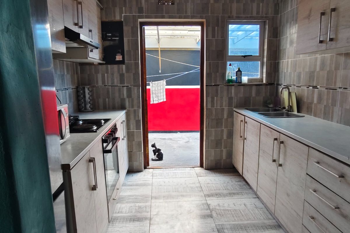 A functional kitchen featuring light wood-look cabinetry, tiled walls and floors, built-in oven and hob, and direct access to an outdoor area.