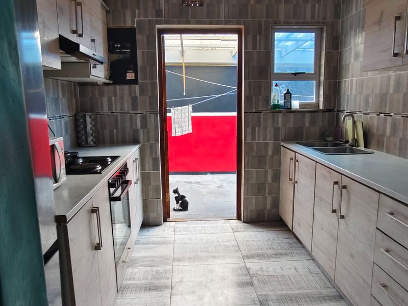 A functional kitchen featuring light wood-look cabinetry, tiled walls and floors, built-in oven and hob, and direct access to an outdoor area.
