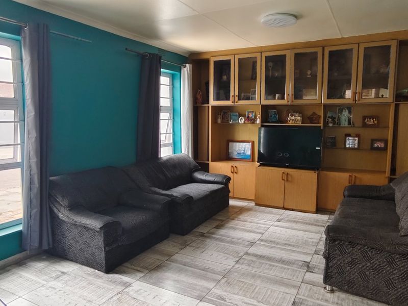 A living room featuring tiled flooring, aluminium window frames, and extensive built-in wooden cabinetry for storage and display.