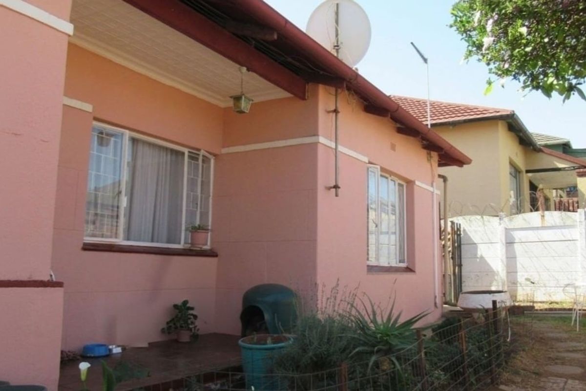 Rear exterior view of the house featuring pink painted walls, security window bars, and a tiled roof structure.