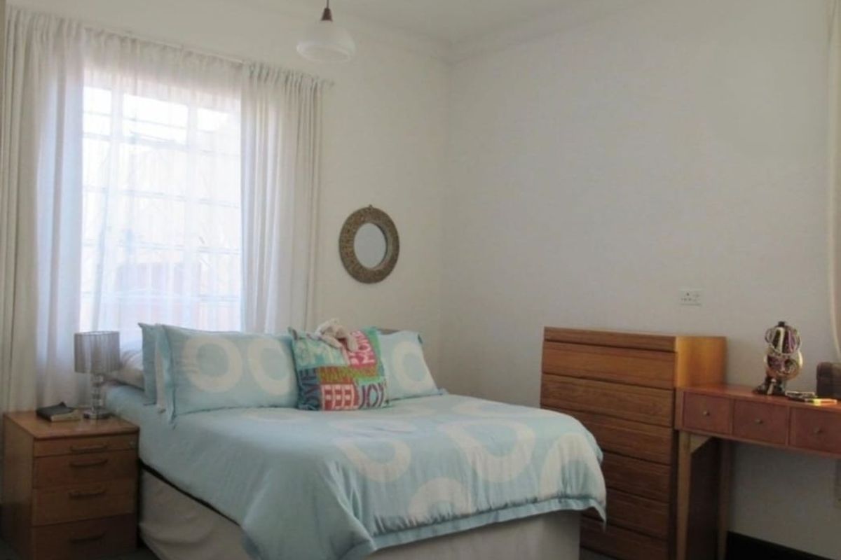 A functional bedroom featuring a ceiling fan, neutral walls, and a window with curtains, providing a comfortable and well-lit living space.