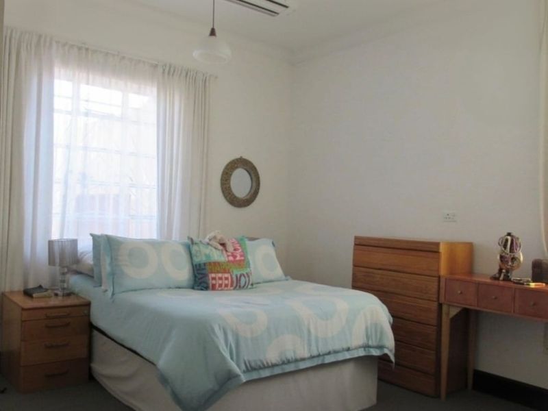 A functional bedroom featuring a ceiling fan, neutral walls, and a window with curtains, providing a comfortable and well-lit living space.