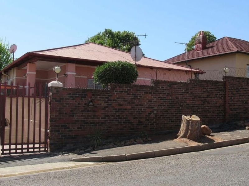Front view of a residential property featuring a brick boundary wall, metal security gate, and a corrugated metal roof.