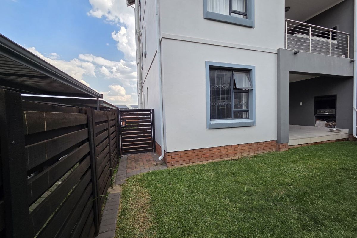 Rear view of the townhouse featuring a private garden, paved walkway, timber fencing, and a covered patio area with a built-in braai.