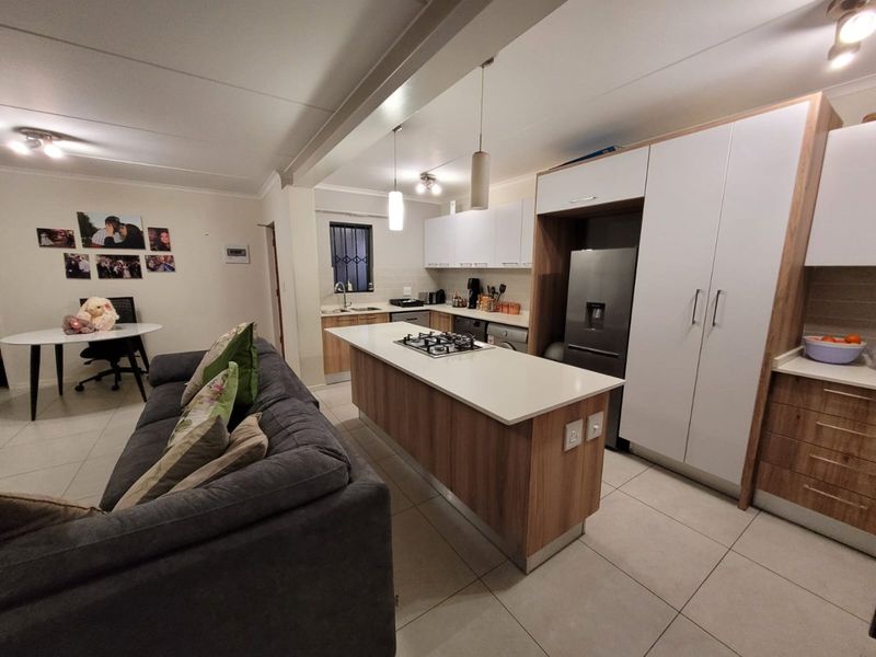 Open-plan living and kitchen area featuring a central island with a gas hob, modern cabinetry, and tiled flooring throughout.