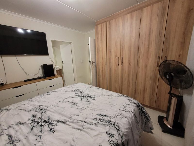 A well-maintained bedroom featuring extensive built-in wooden cupboards, neutral tiled flooring, and clean finishes throughout.