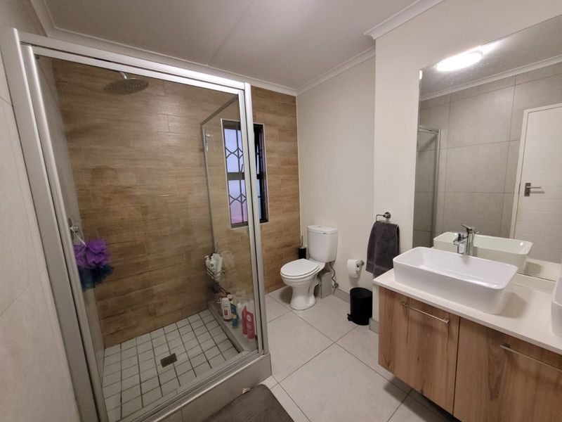 Modern bathroom featuring a glass-enclosed shower with wood-look accent tiling, a contemporary vessel sink vanity, and neutral floor tiles.