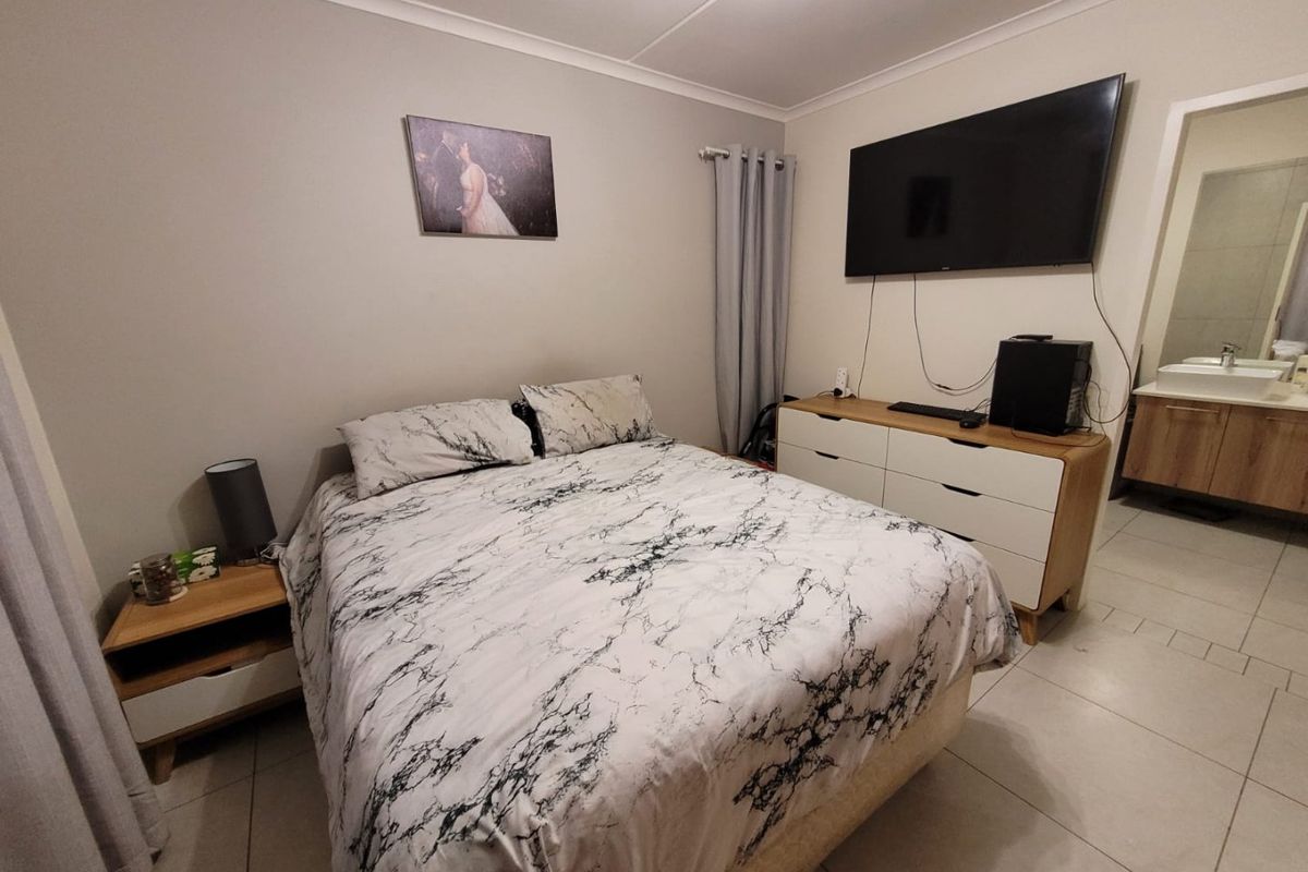 A well-maintained bedroom featuring tiled flooring, cove cornicing, and direct access to an en-suite bathroom.
