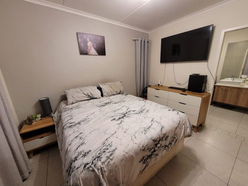 A well-maintained bedroom featuring tiled flooring, cove cornicing, and direct access to an en-suite bathroom.